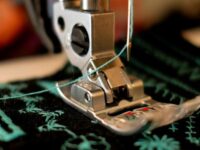 Close-up of a sewing machine foot creating embroidered designs on dark fabric