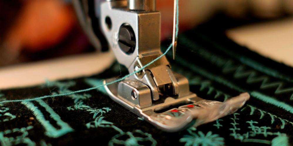 Close-up of a sewing machine foot creating embroidered designs on dark fabric