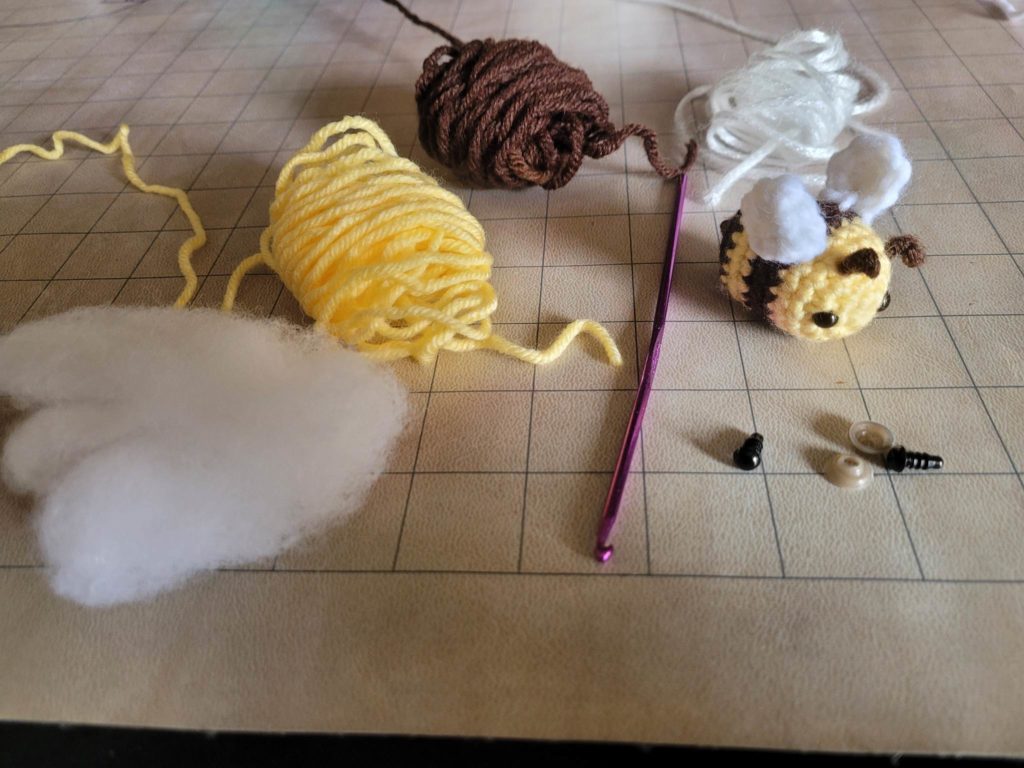 Yellow and brown yarn unraveled on a table with a crochet hook, some stuffing, and a partially completed crocheted mini-stuffed animal.