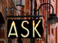 Light up neon sign on a street: "ASK"