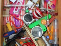 A junk drawer full of miscellaneous items: tape measure, super glue, sunglasses, dice.