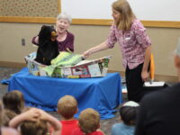 Two librarians give a presentation with puppets to an enthralled audience of children and adults